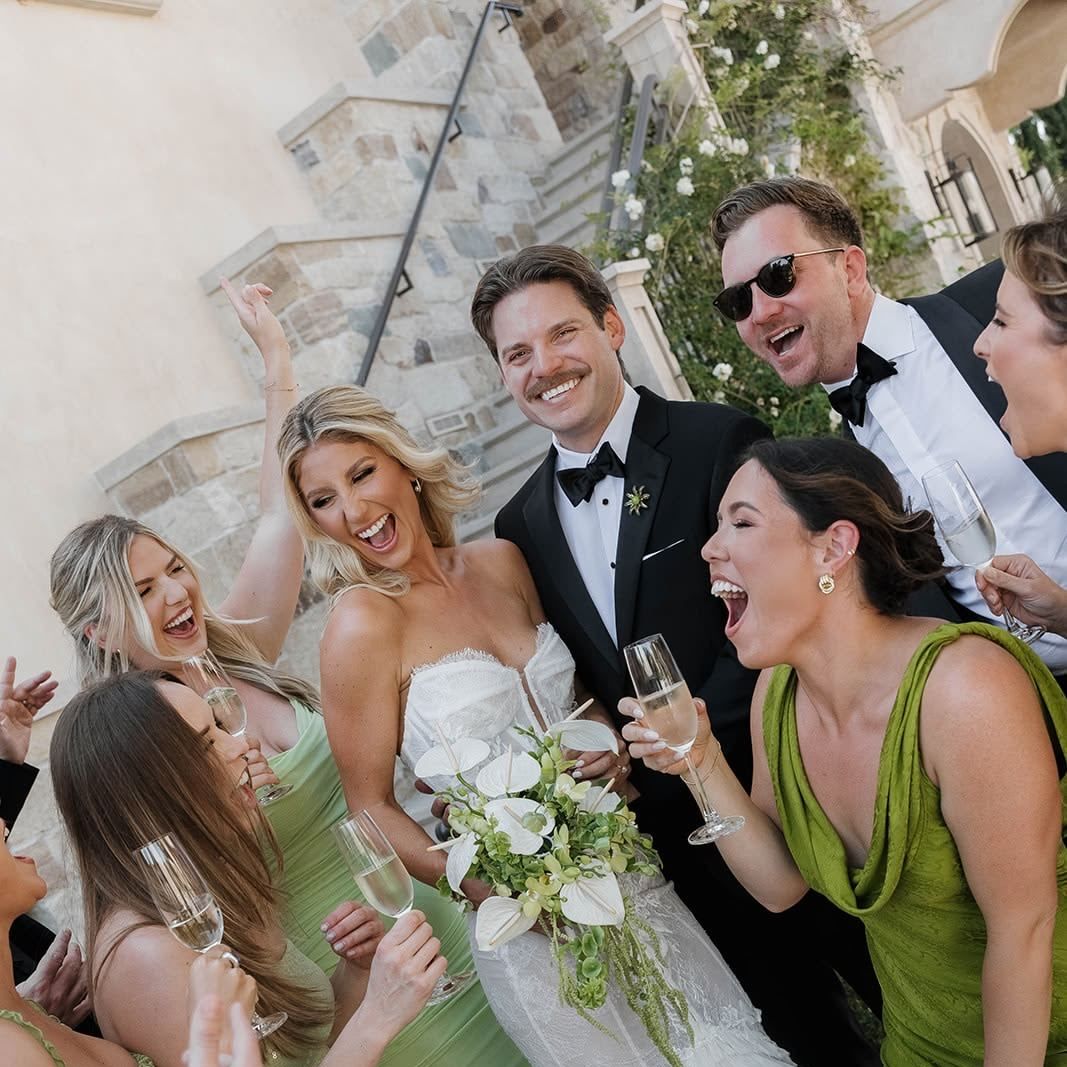 The bride, groom and wedding party laughing together with champagne